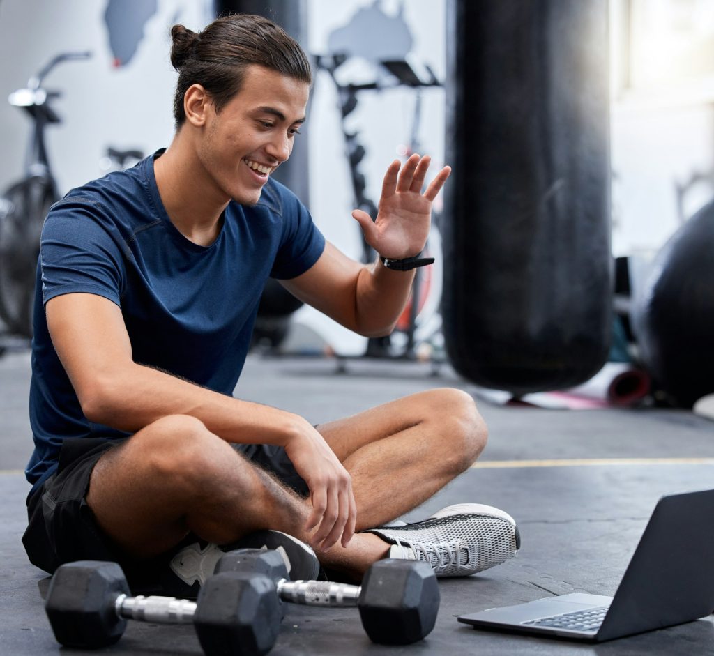 Man, laptop and wave for video call in gym with smile rest on floor after training session. Guy, we